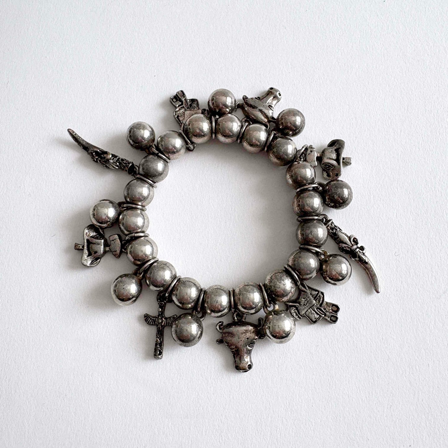 Vintage silver-tone Southwestern charm stretch bracelet with beaded design and dangling Western-inspired charms on white background