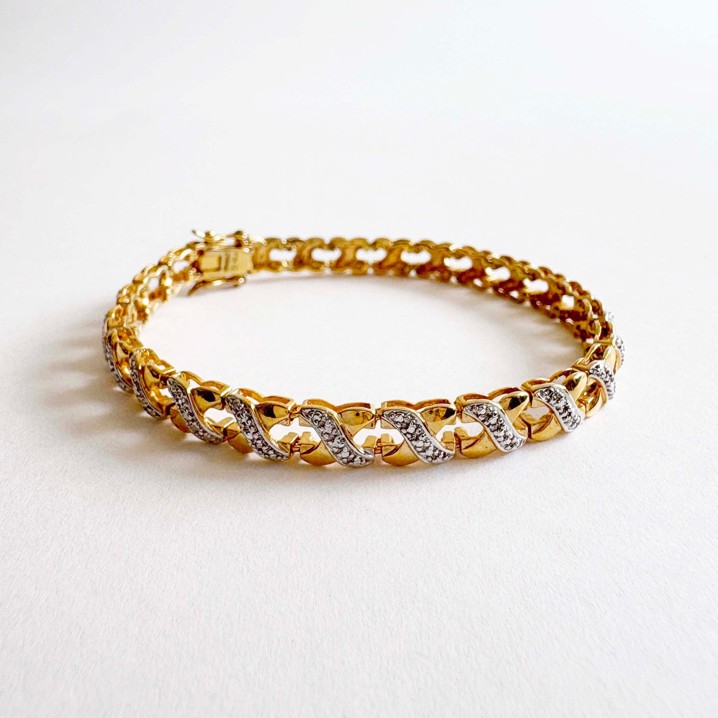 Gold bracelet with interwoven X-link design on a white background