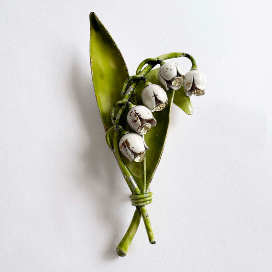 Vintage Lisner lily of the valley brooch with white enamel flowers, green leaves, and rhinestone accents from the 1960s.