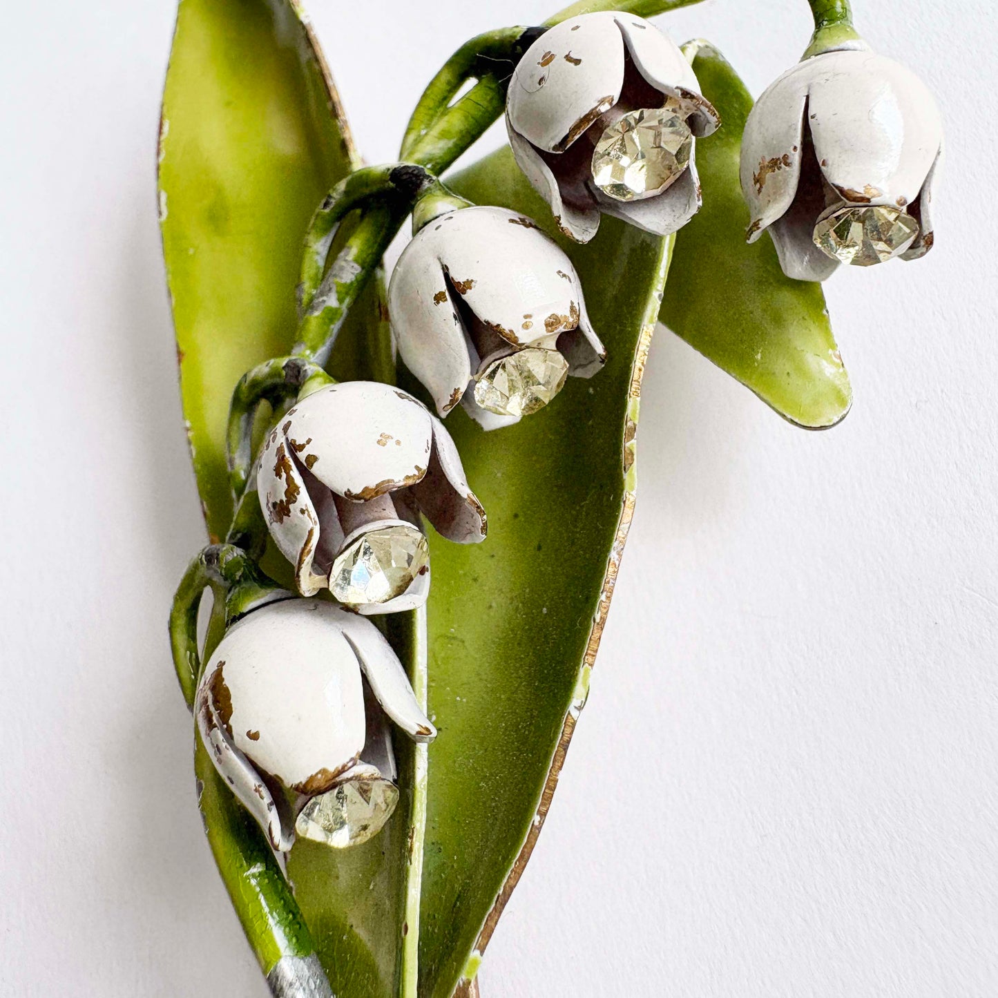 Vintage Lisner lily of the valley brooch with white enamel flowers, green leaves, and rhinestone accents from the 1960s.