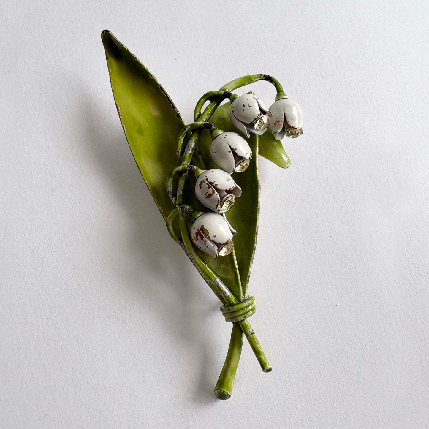 Vintage Lisner lily of the valley brooch with white enamel flowers, green leaves, and rhinestone accents from the 1960s.