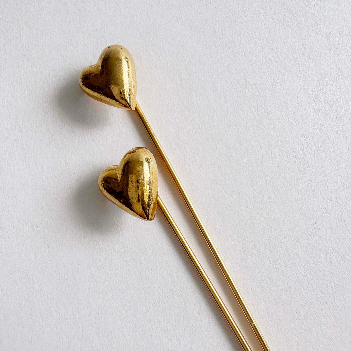 Pair of vintage gold-tone heart stick pins with long slender needles on white background