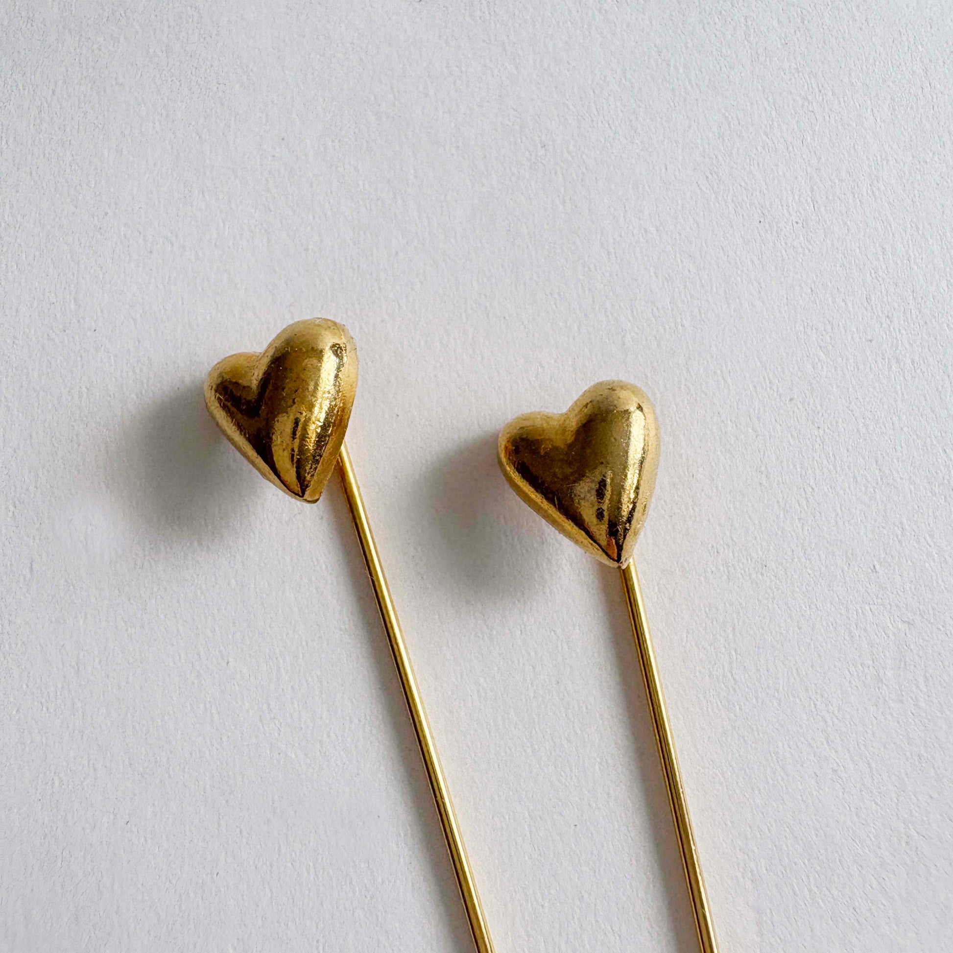 Pair of vintage gold-tone heart stick pins with long slender needles on white background