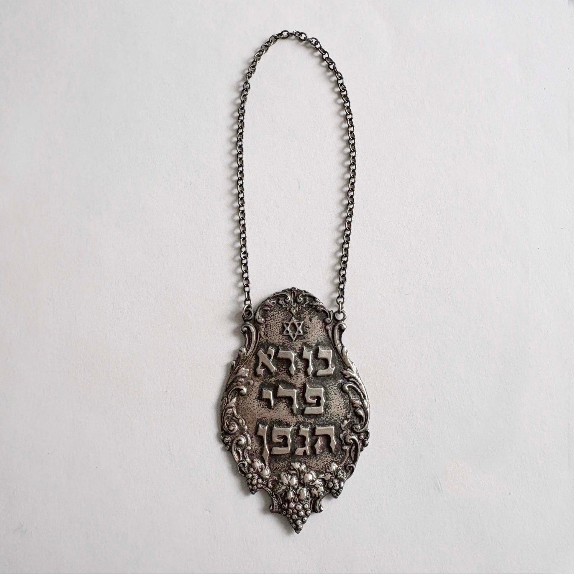 Sterling silver Judaica Shabbat wine bottle tag with Hebrew inscription and decorative chain on white background