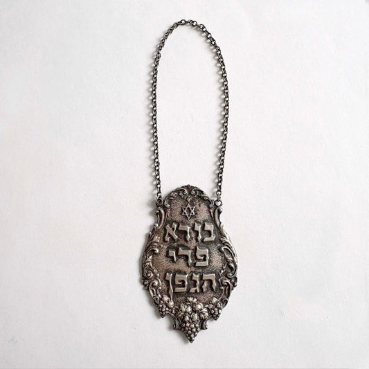 Sterling silver Judaica Shabbat wine bottle tag with Hebrew inscription and decorative chain on white background