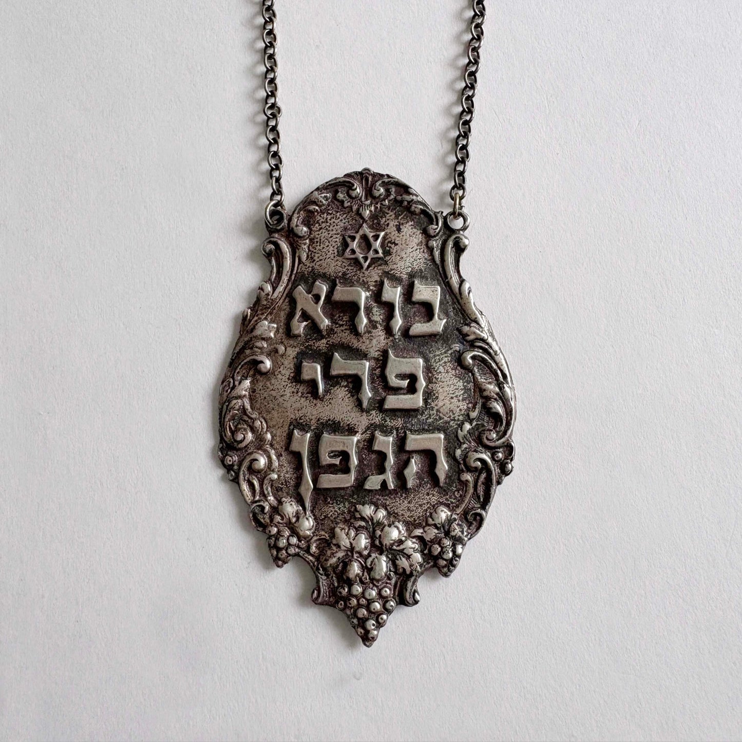 Sterling silver wine bottle tag with an ornate Hebrew text and start of David on a light gray background