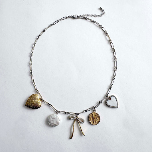 Silver chain charm necklace with gold heart locket, crystal bow, love coin and mother of pearl heart charms on white background