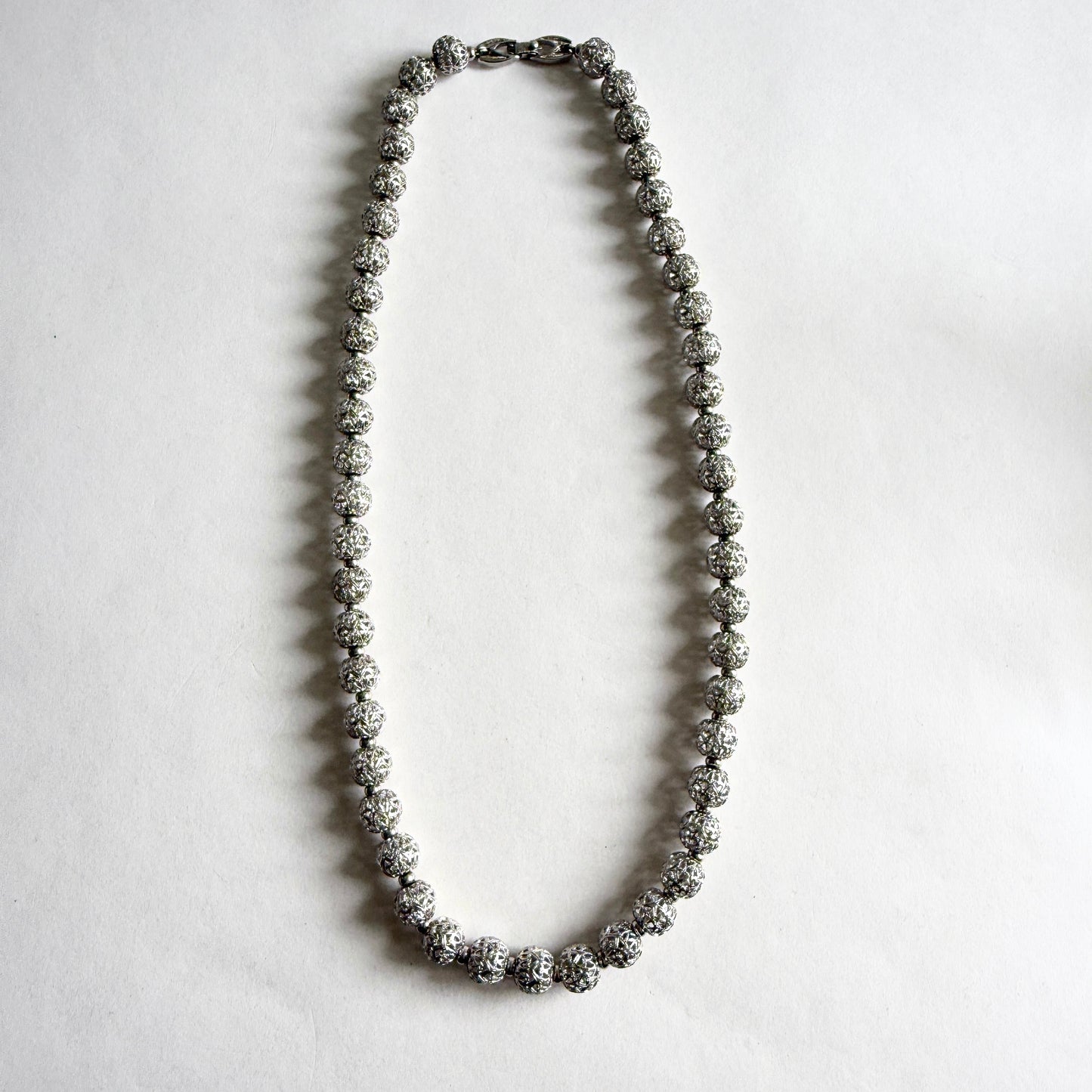 A full-length view of a vintage Monet silver-tone necklace consisting of uniform filigree beads, presented on a clean white background.