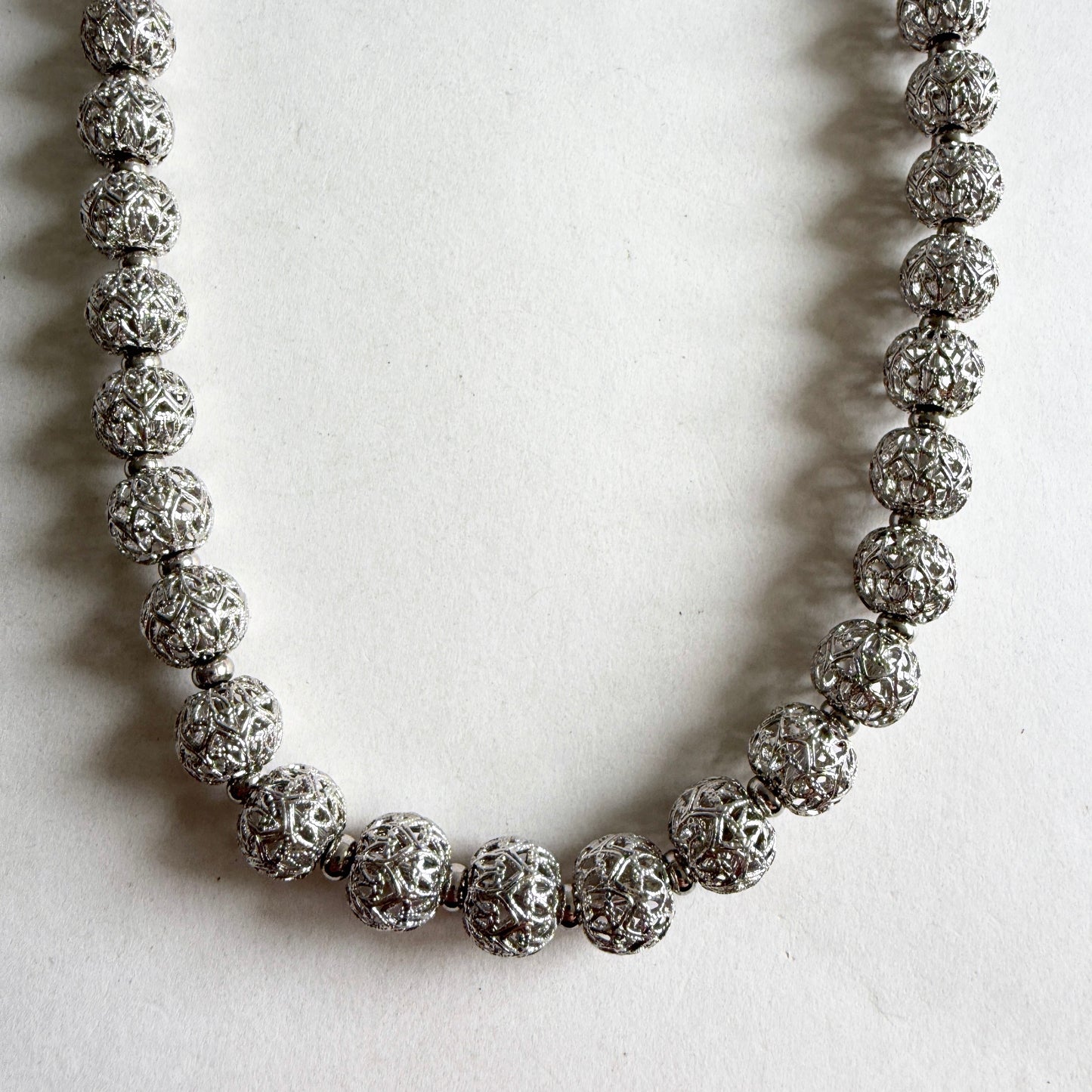 A close-up shot showing the intricate openwork lace pattern of the silver-tone filigree beads and the polished spacers.