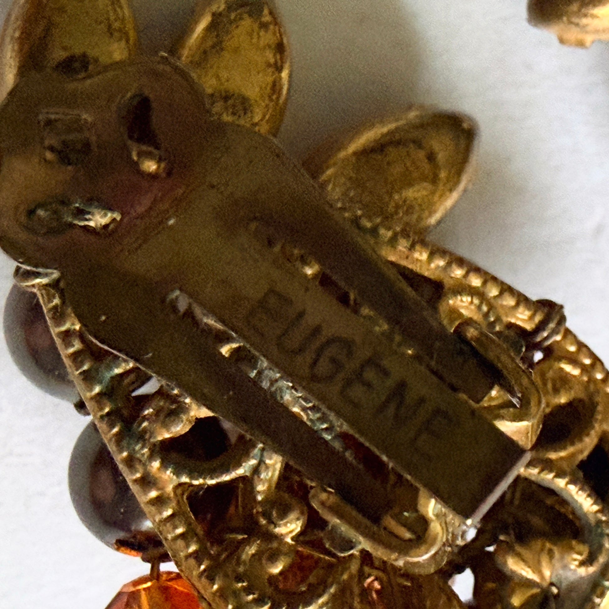 Close-up archival photograph of the "EUGENE" signature hallmark stamped on the gold-tone metal earring clip.