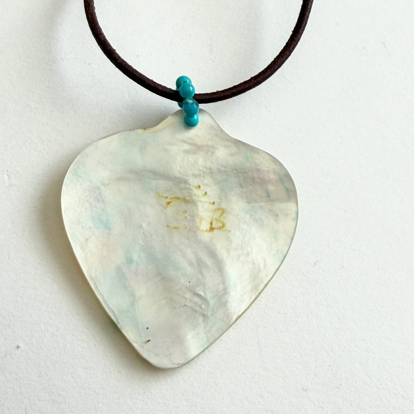 Shell pendant on a black cord with a blue accent bead against a white background