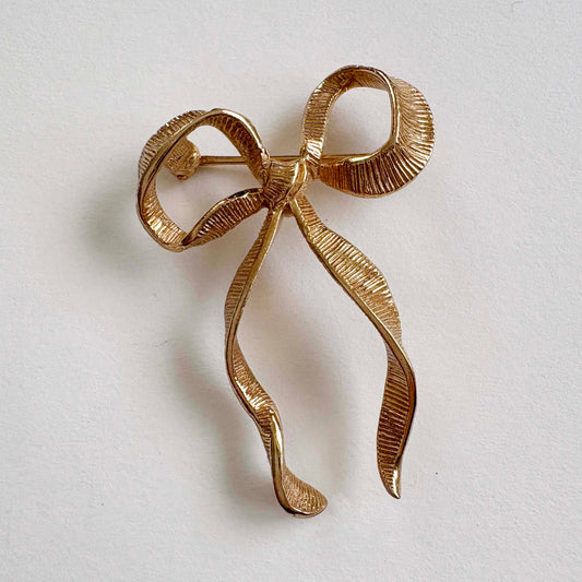 gold bow-shaped brooch on a light gray background