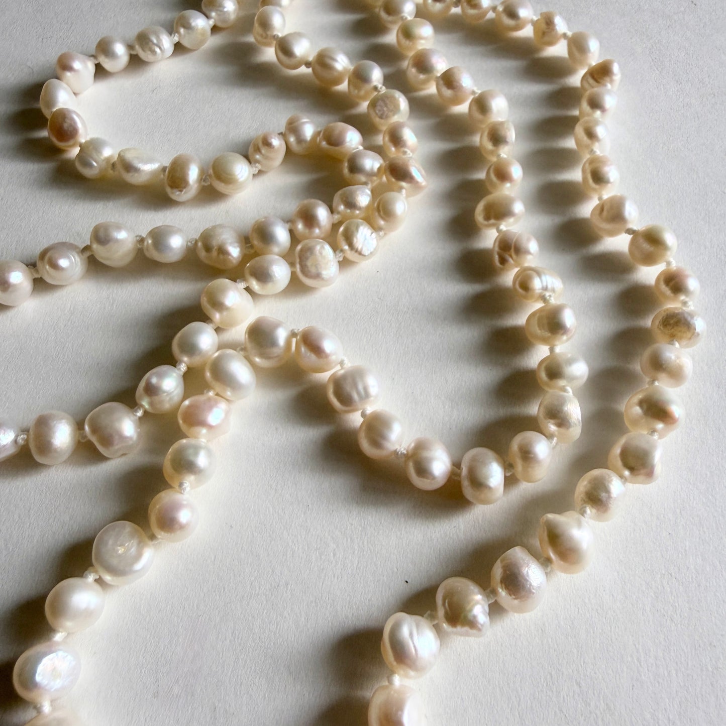 Macro detail of high-luster white baroque freshwater pearls, showcasing the unique organic nugget-like shapes and hand-knotted silk thread.