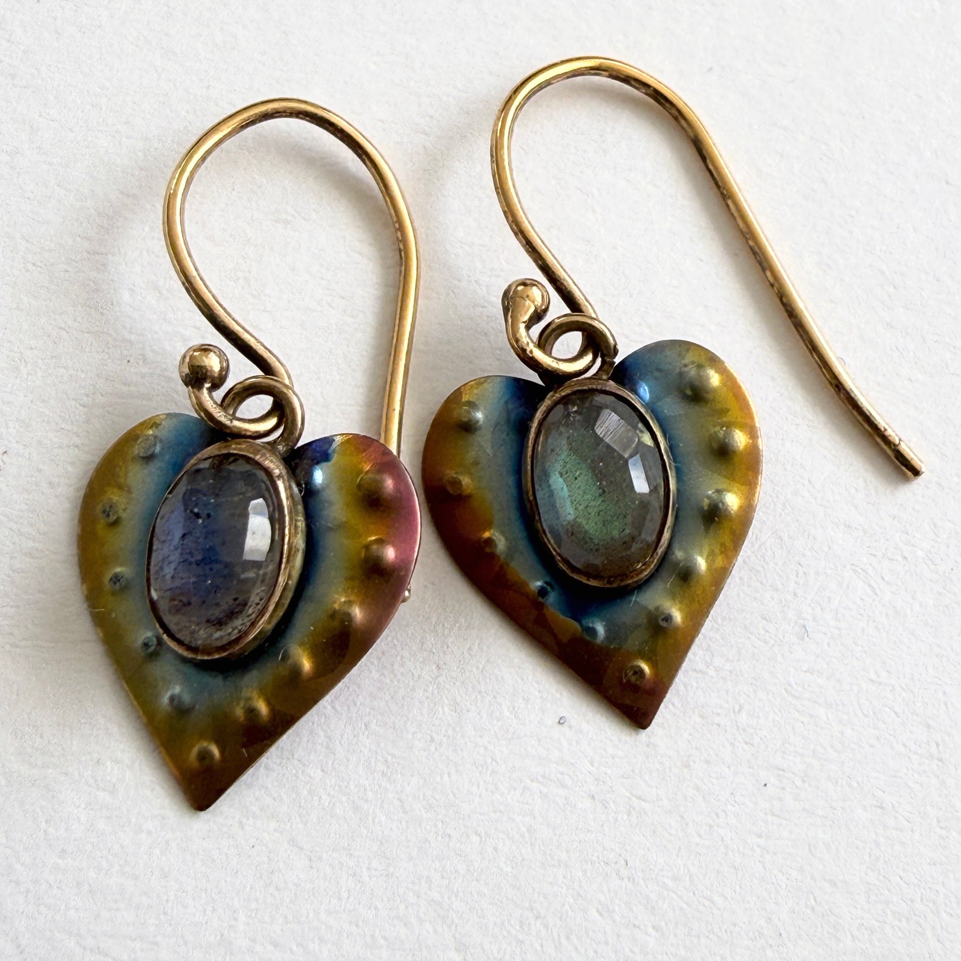 Heart-shaped earrings with metallic finish and gemstones on a white background