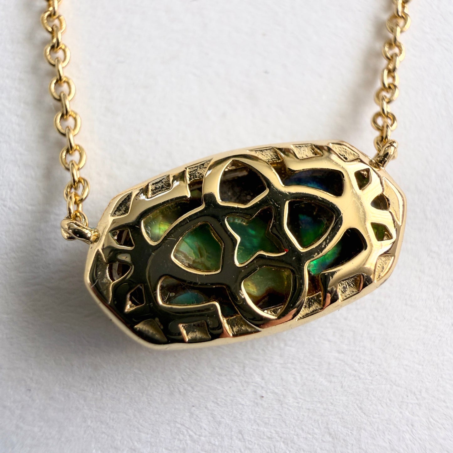 Gold necklace with a green stone pendant on a white background