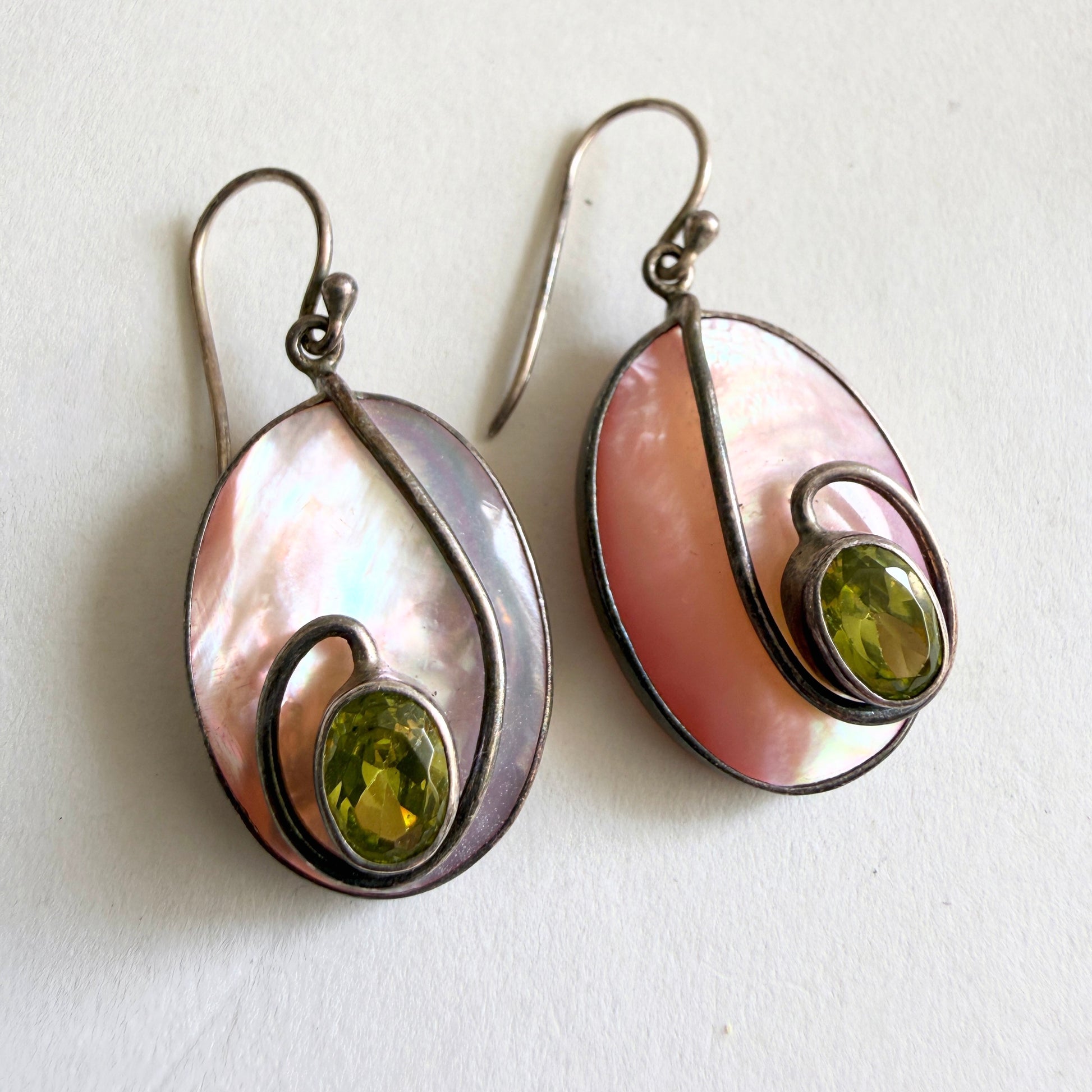 Front view of the 'Algae Bloom' earrings featuring iridescent blush mother-of-pearl slabs with asymmetrical sterling silver ribbons.