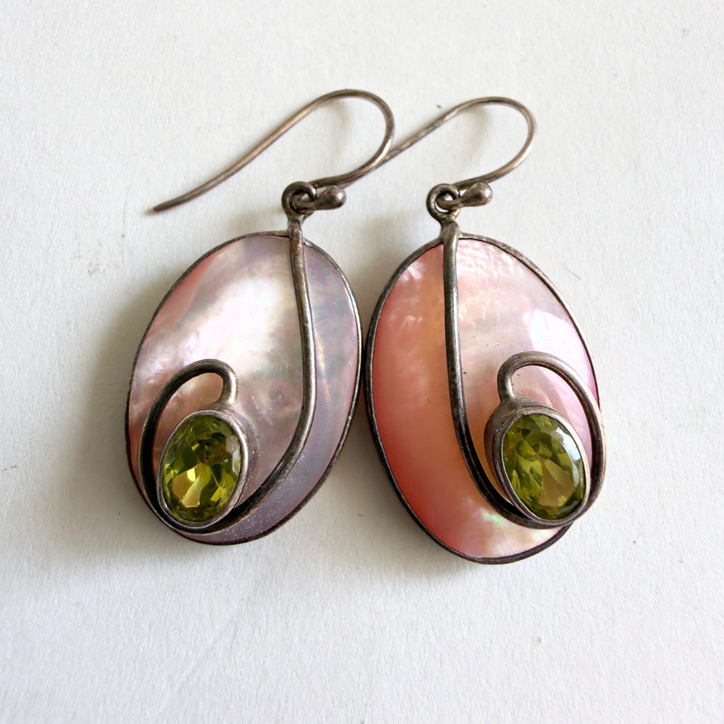 Close-up of the faceted olive-green peridot stone set against the soft rose and ivory nacre of the shell.