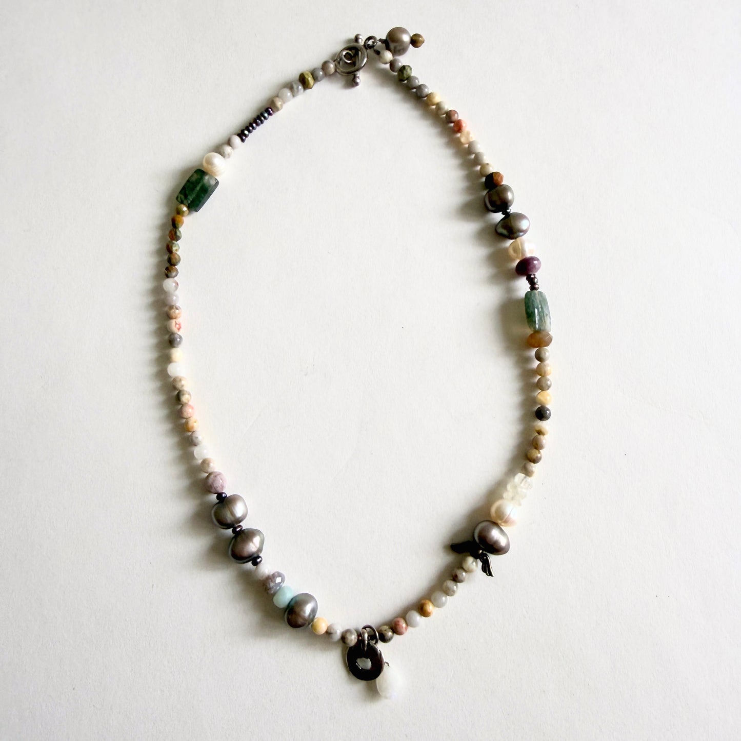A 17-inch artisan necklace featuring asymmetrical peacock grey baroque pearls, earth-tone jasper, and a sterling silver moonstone pendant.