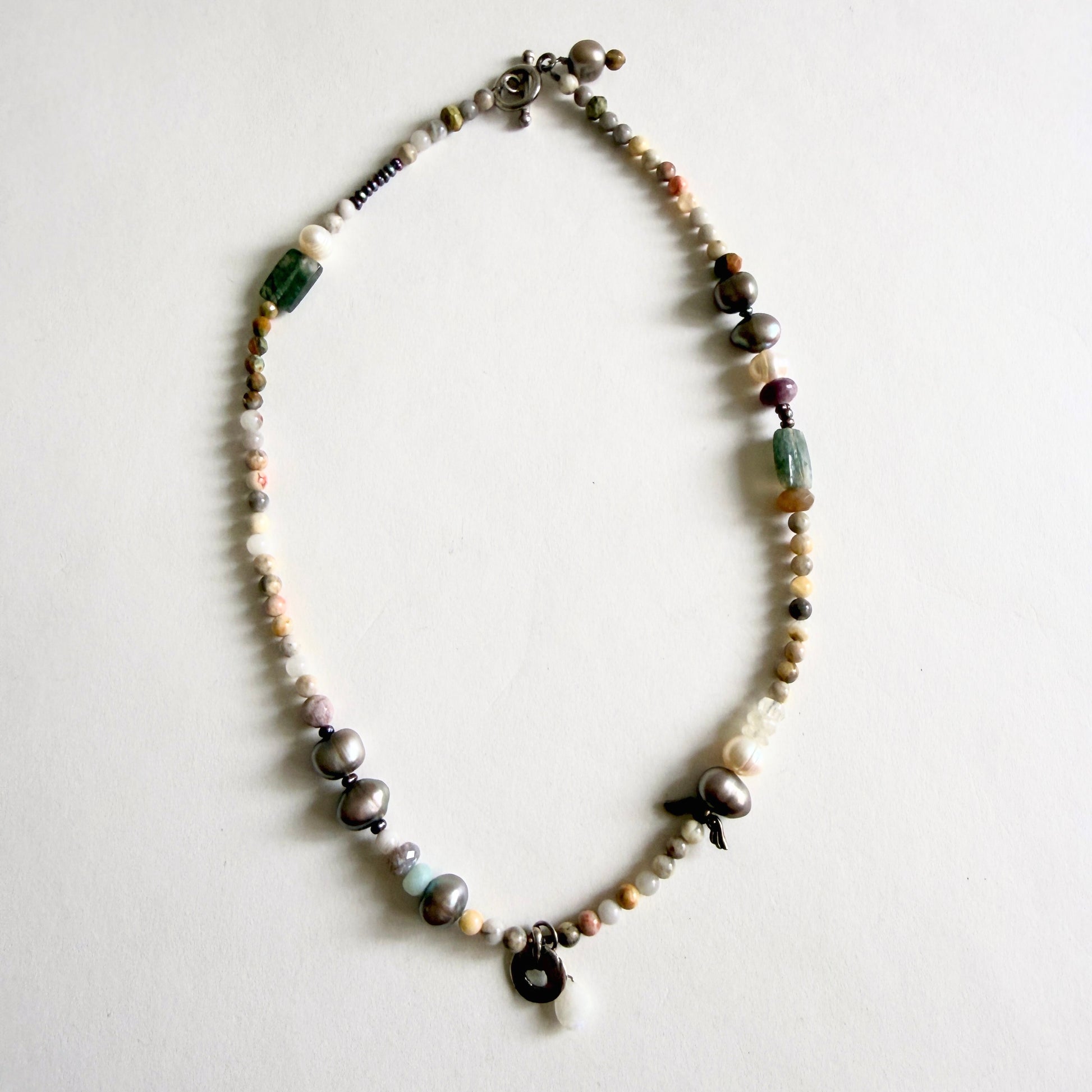A 17-inch artisan necklace featuring asymmetrical peacock grey baroque pearls, earth-tone jasper, and a sterling silver moonstone pendant.