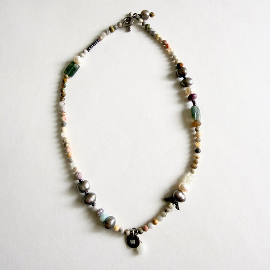 A 17-inch artisan necklace featuring asymmetrical peacock grey baroque pearls, earth-tone jasper, and a sterling silver moonstone pendant.