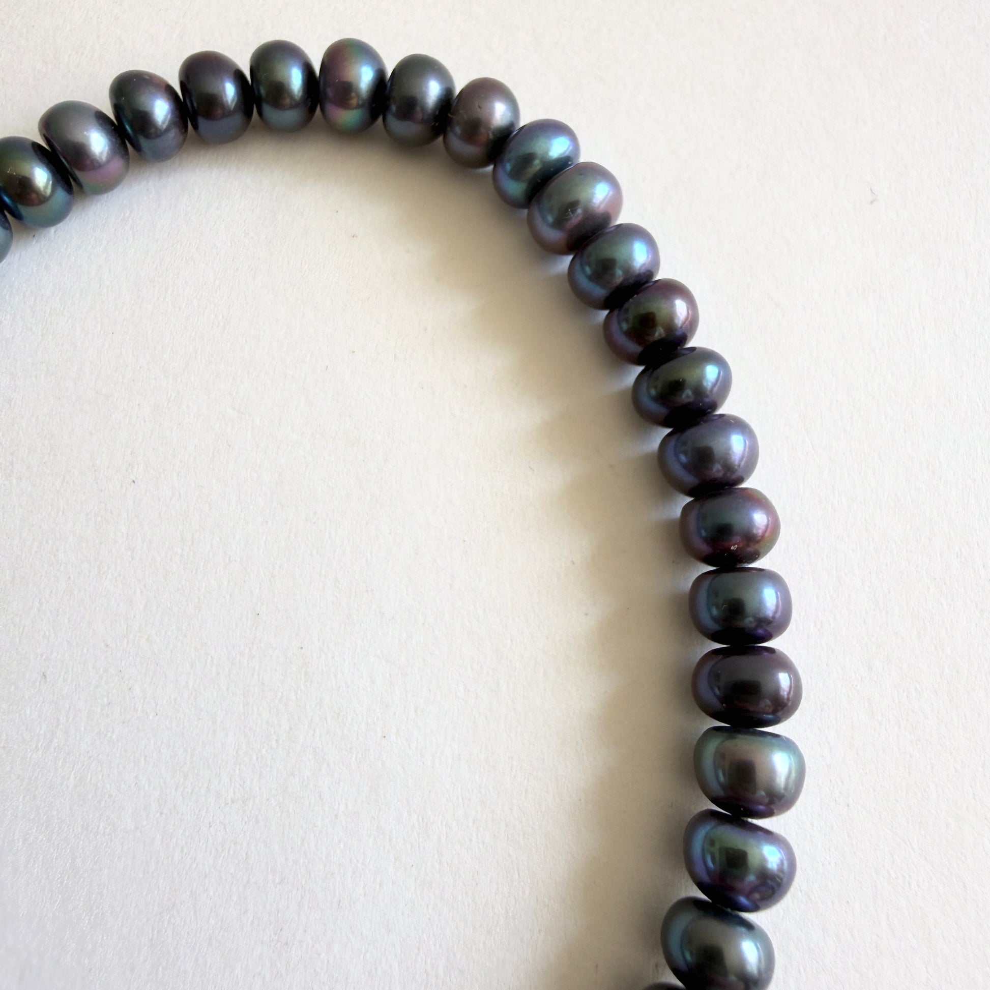 Macro detail of the peacock pearls, showing the high-luster 'orient' with shifts of forest green, midnight blue, and violet.