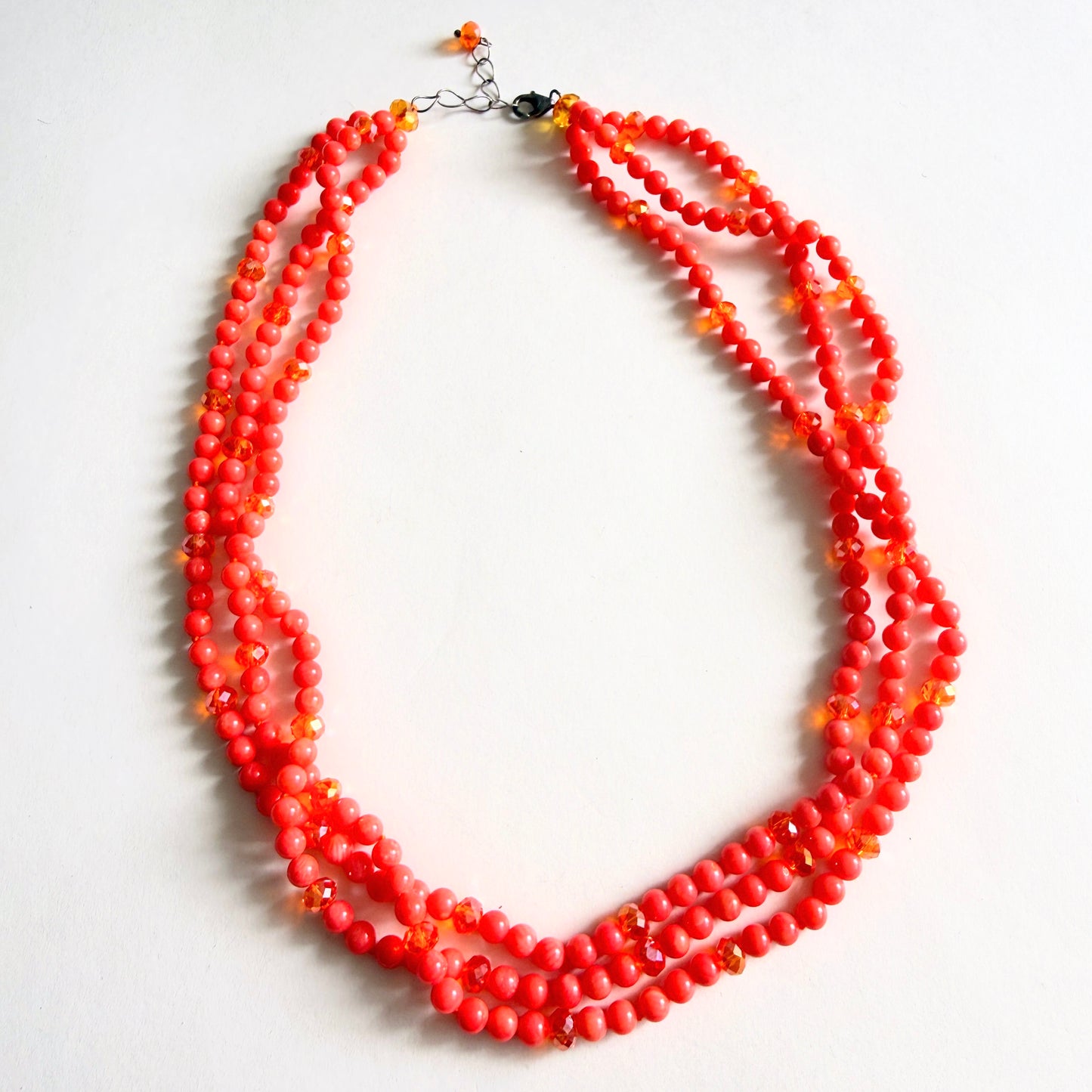 Full view of a multi-strand necklace featuring vibrant orange-red dyed bamboo coral branch beads accented with faceted amber glass spacers and a sterling silver lobster clasp.