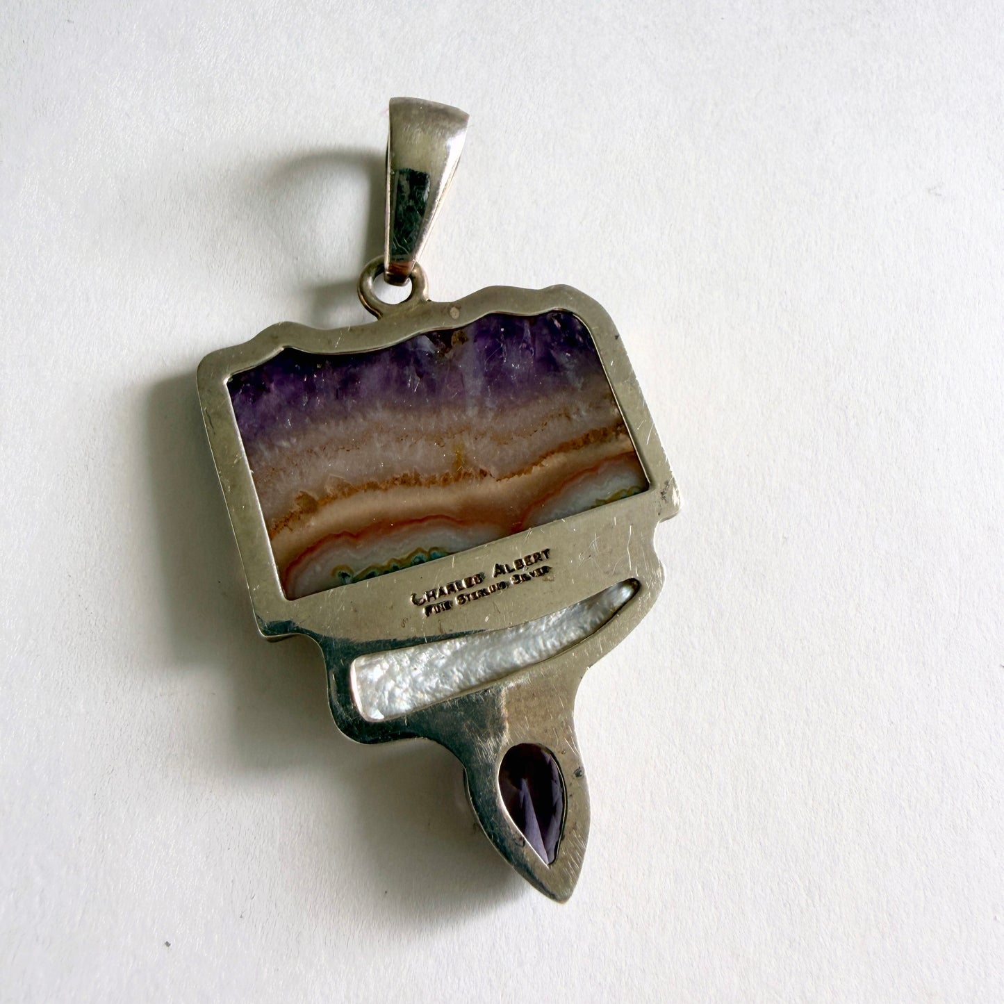 Detailed view of the luminous baroque pearl and the precision-faceted amethyst drop suspended in a sculptural silver setting.