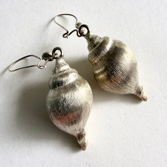 A pair of hand-fabricated sterling silver conch shell drop earrings, featuring a high-luster moonlight patina on a white background.