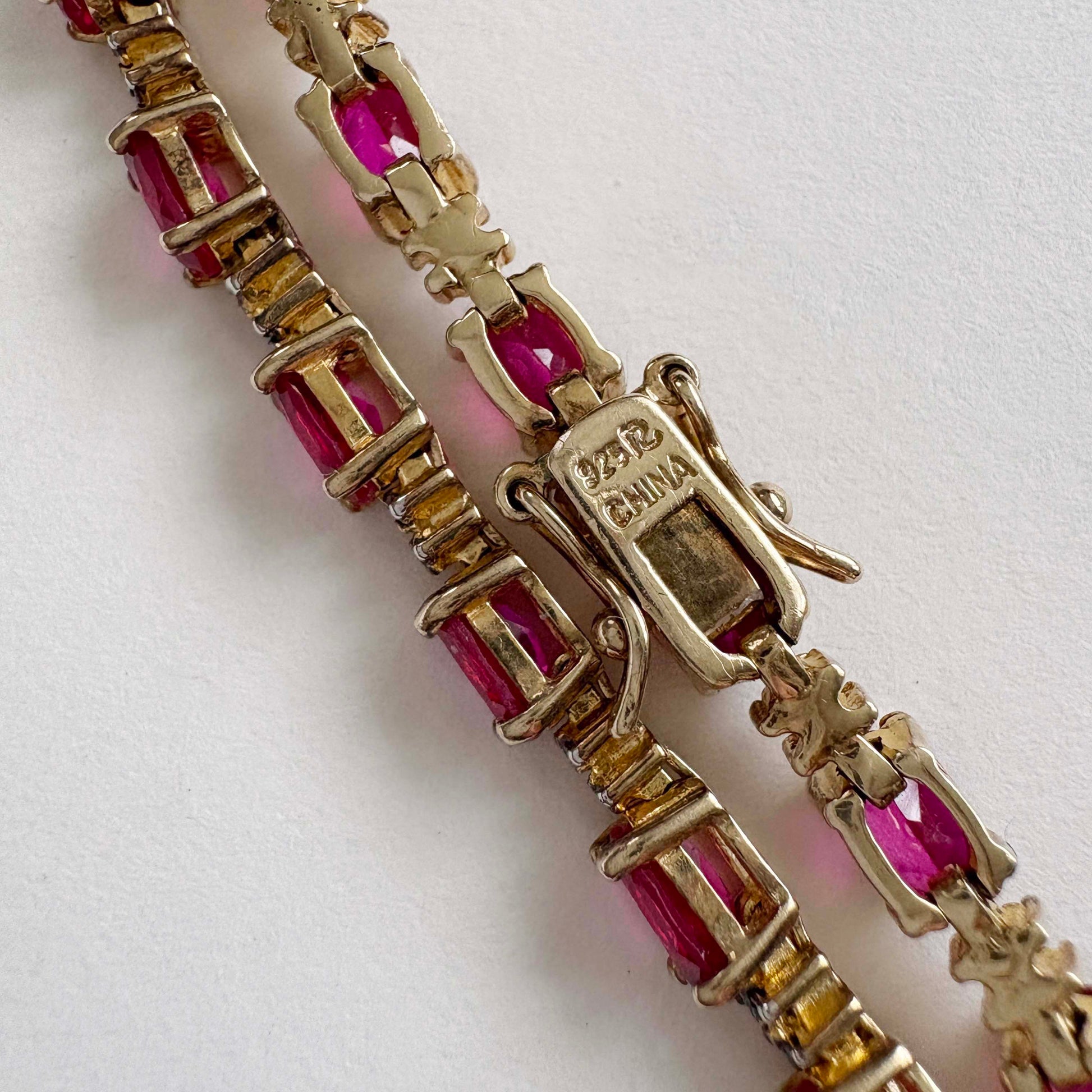 gold bracelet with pink gemstones on a white background