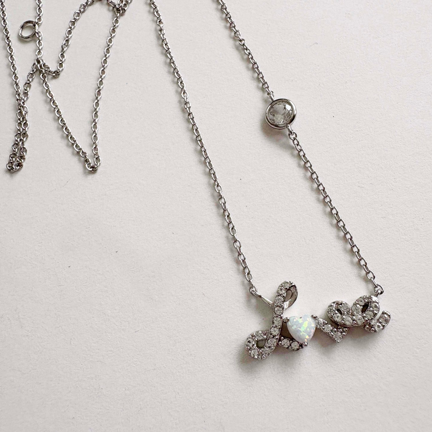 Silver necklace with a Love script pendant on a light gray background