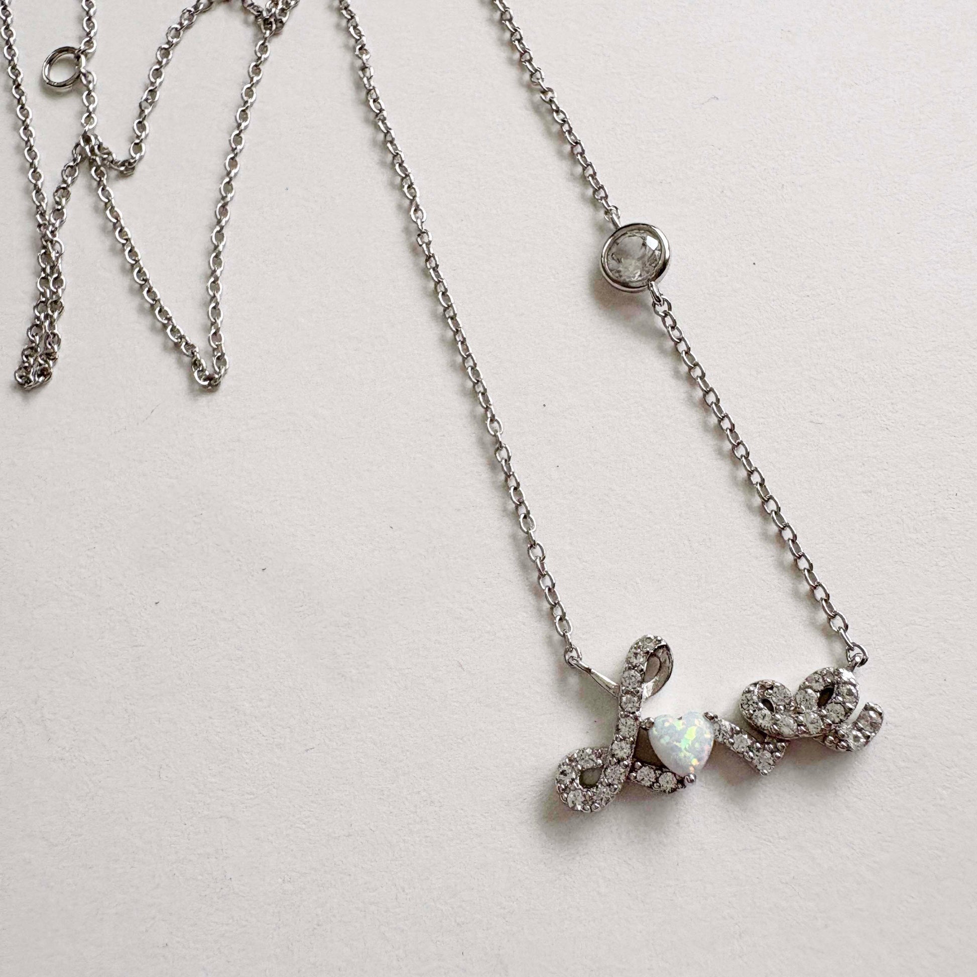 Silver necklace with a Love script pendant on a light gray background