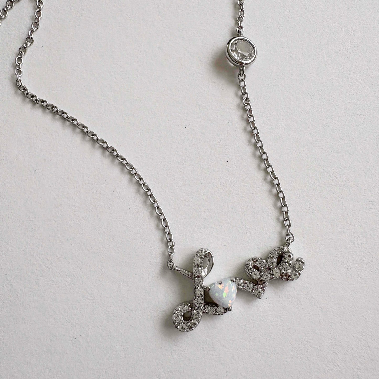 Silver necklace with a Love script pendant on a light gray background