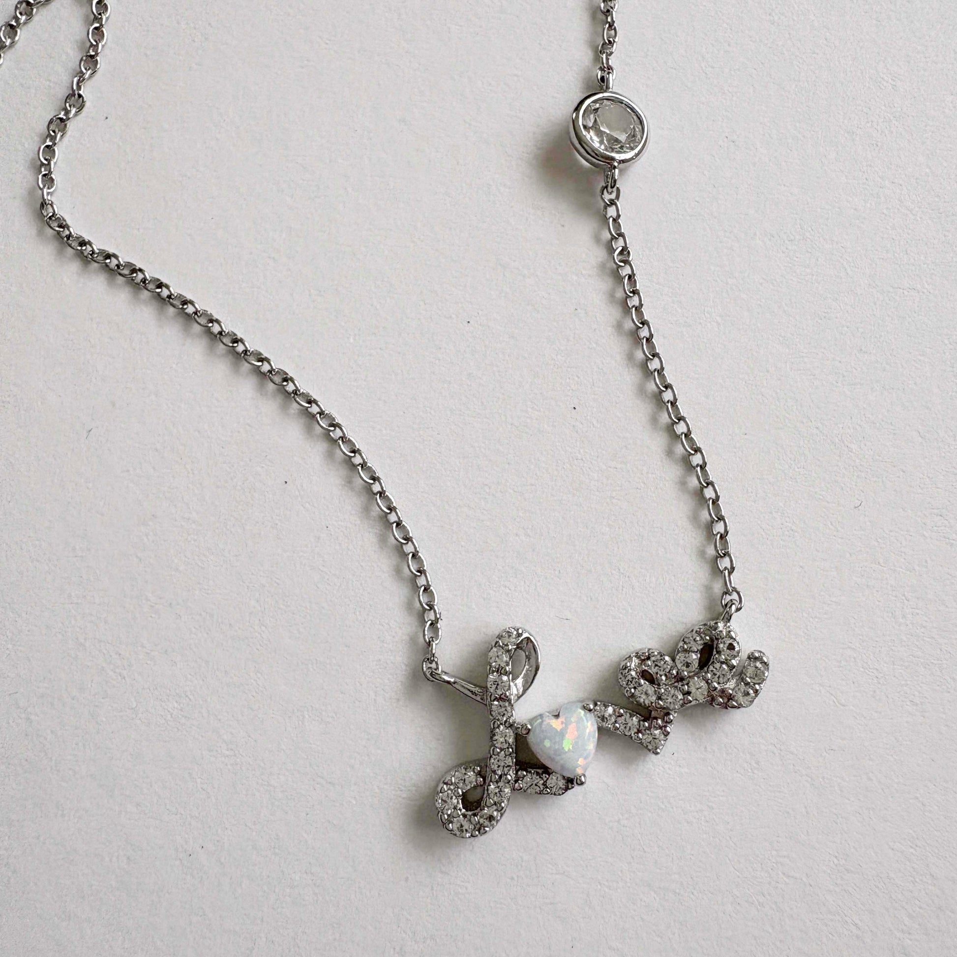 Silver necklace with a Love script pendant on a light gray background