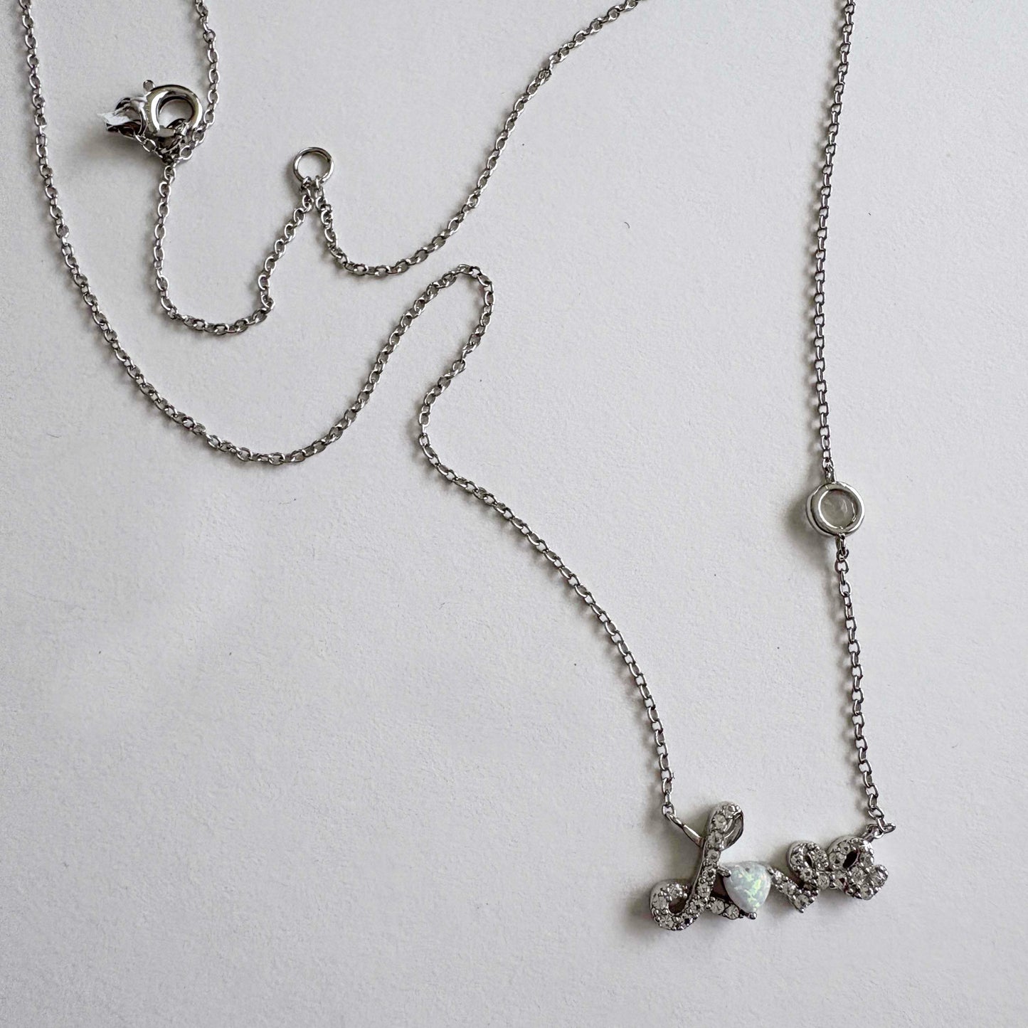 Silver necklace with a Love script pendant on a light gray background
