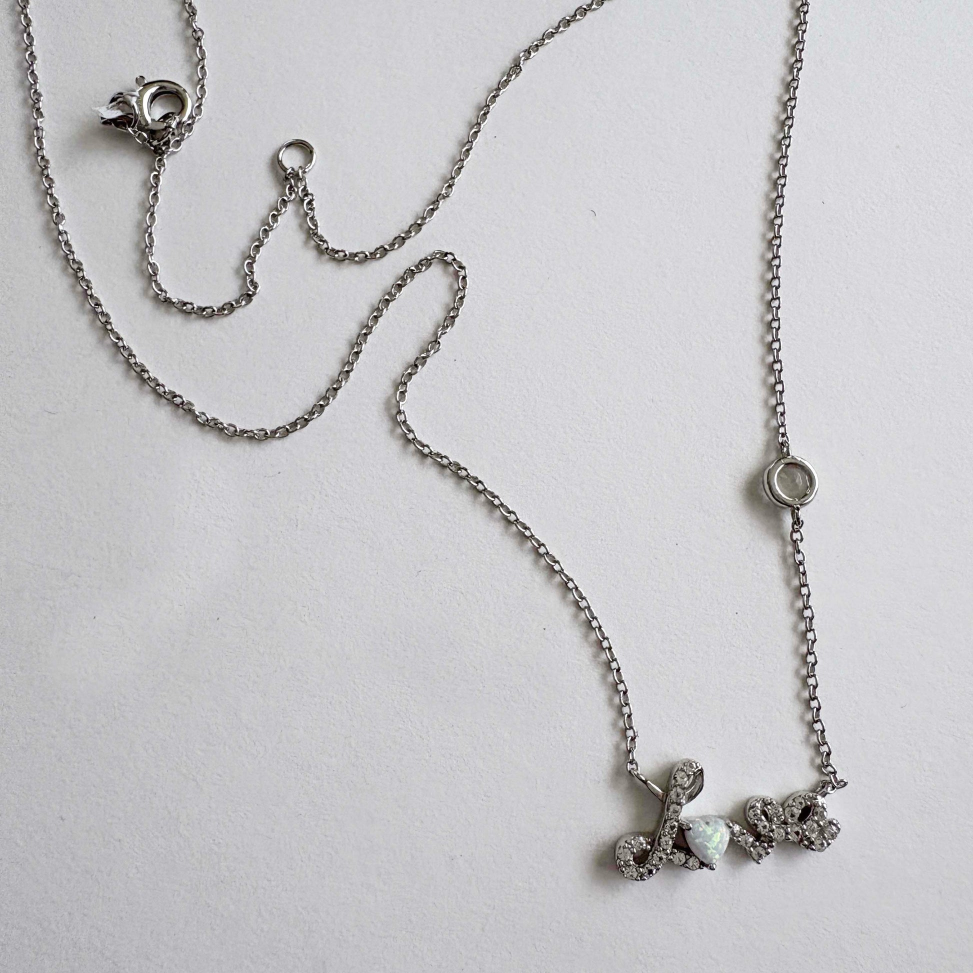 Silver necklace with a Love script pendant on a light gray background