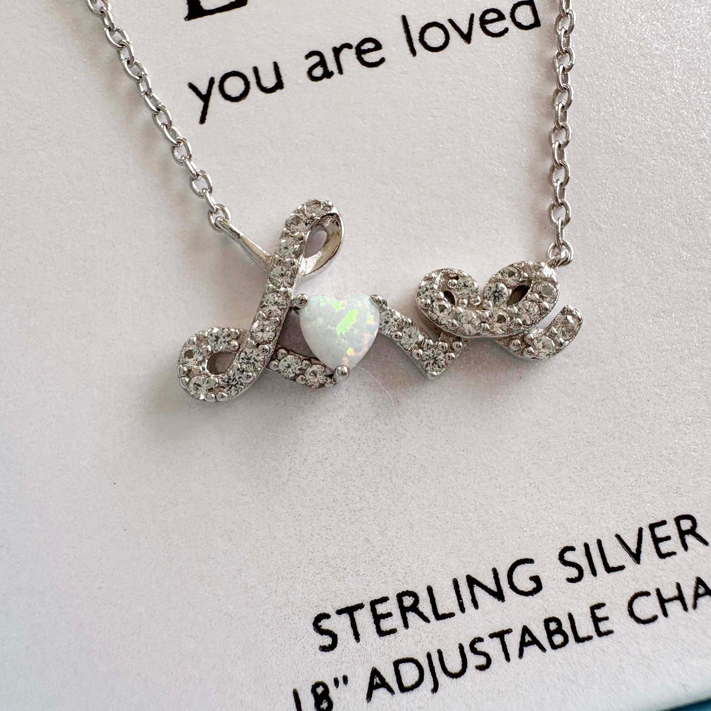 Silver 'LOVE' necklace with opal stone on a card with text