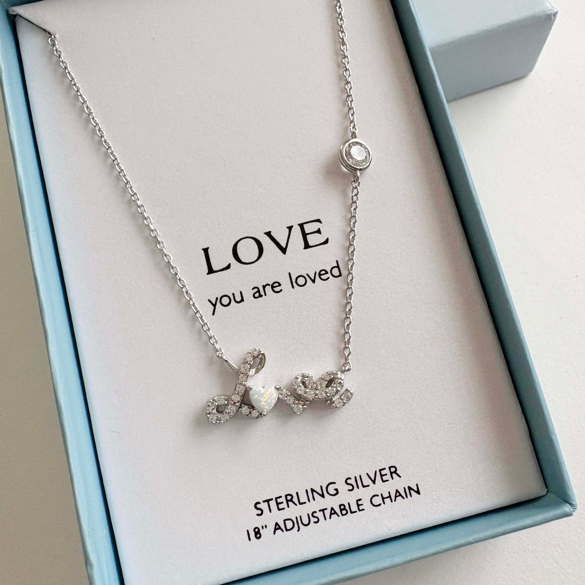 Silver necklace with a Love script pendant on a card on a light gray background