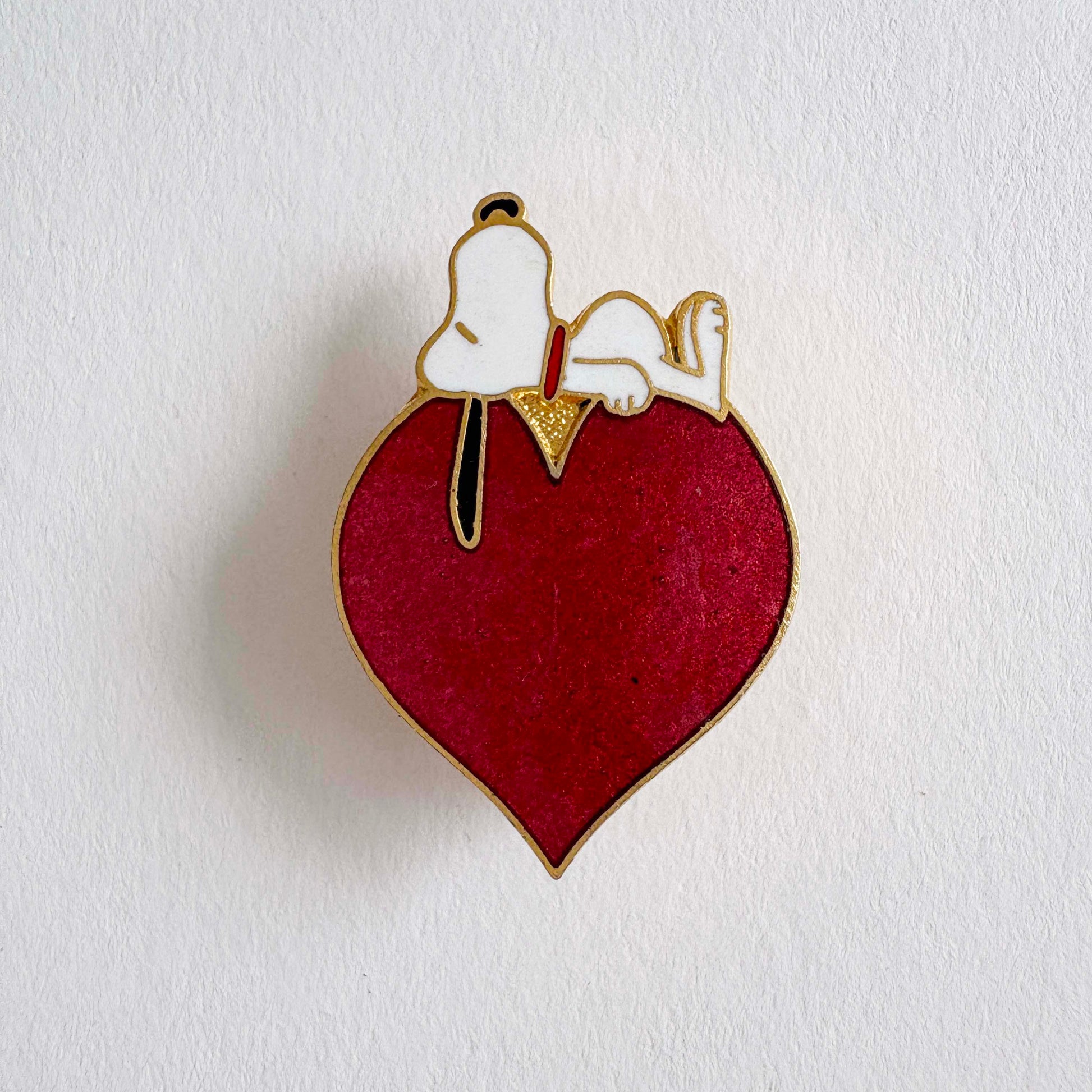 Enamel pin with a snoopy dog on a red heart against a white background