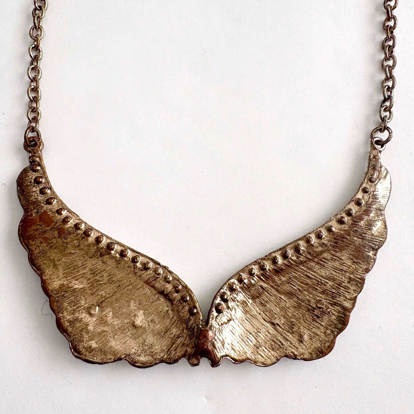 Reverse side of winged bronze pendant necklace on a white background